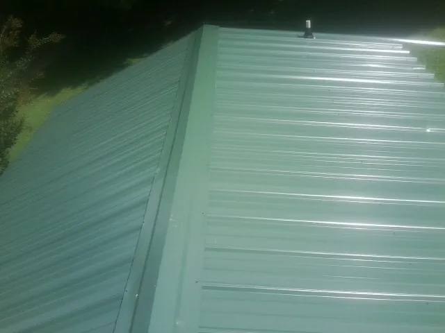 New green metal panels meeting at the ridge of a roof — Flat Roof Repair work by our crew in Alachua