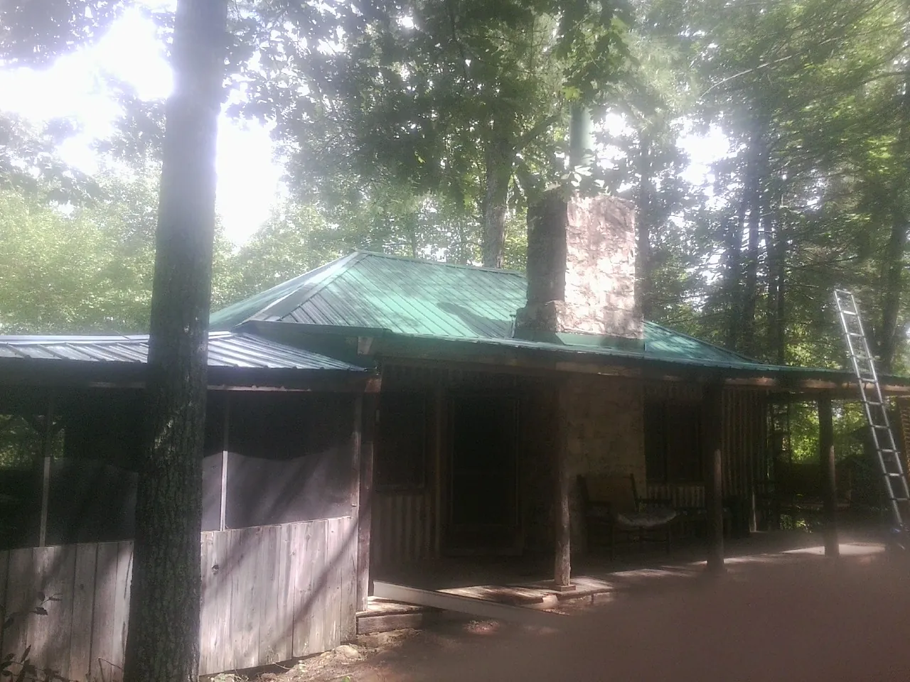 Green metal roof and stone chimney above a log cabin porch in Alachua