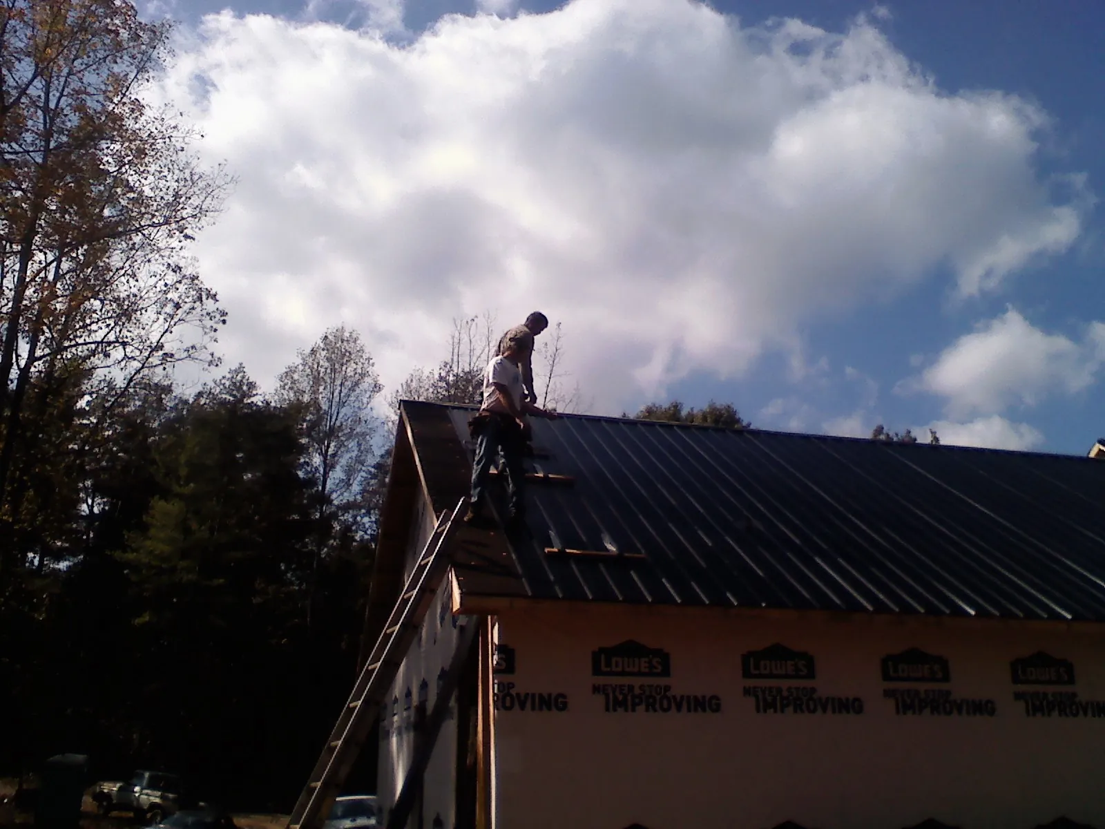 Roofer fastening dark metal panels high against a cloudy sky, from a Roof Inspection job in Alachua