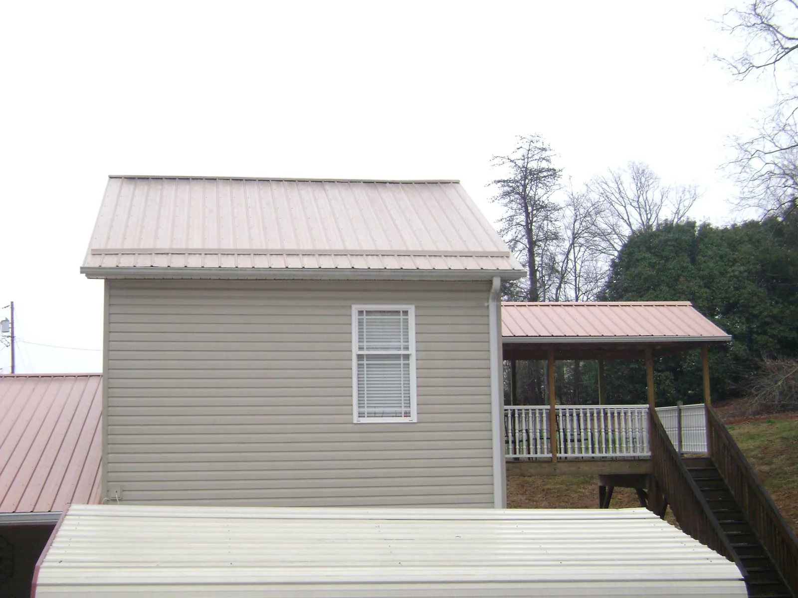 Tan metal roofs on a two story addition and attached porch, from a Roof Replacement job in Alachua